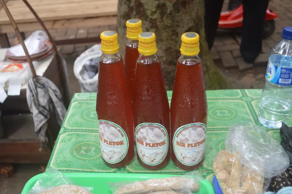 Gelas berisi bir pletok merah dengan botol di sampingnya, minuman rempah khas Betawi