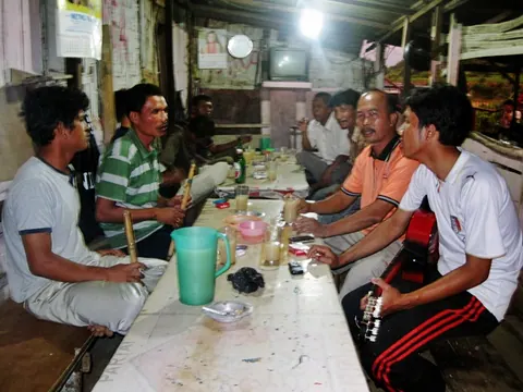 Suasana lapo tuak: orang-orang duduk di bangku kayu sambil minum tuak dan bercakap